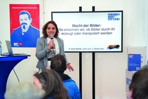 Isabel Lerch hält einen Workshop im FES-Zelt. Auf einem Bildschirm neben ihr steht "Macht der Bilder: so erkennen wir, ob Bilder durch KI erzeugt oder manipuliert wurden"