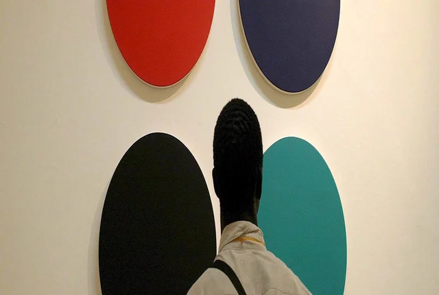 Ein Mann steht mit dem Rücken zur Kamera und schaut sich ein Gemälde mit vier verschiedenfarbigen Kreisen an.