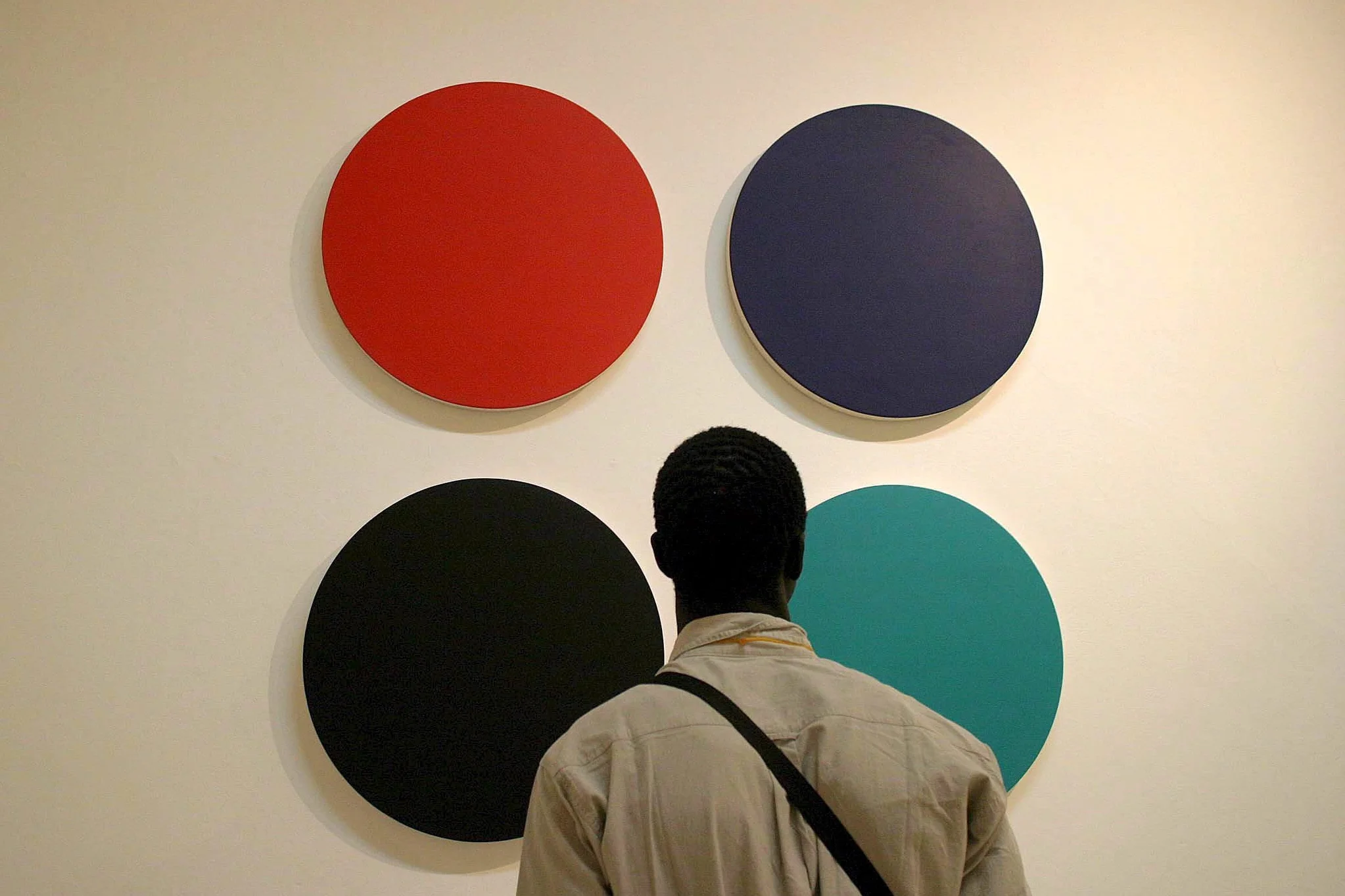 Ein Mann steht mit dem Rücken zur Kamera und schaut sich ein Gemälde mit vier verschiedenfarbigen Kreisen an.