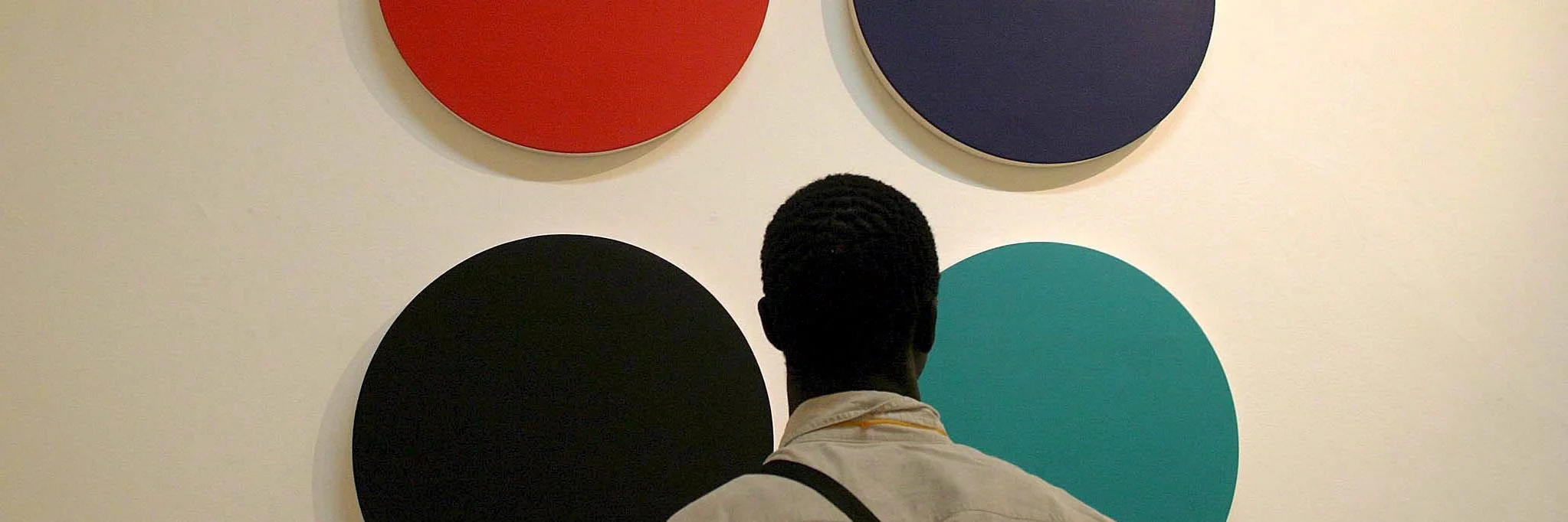 Ein Mann steht mit dem Rücken zur Kamera und schaut sich ein Gemälde mit vier verschiedenfarbigen Kreisen an.