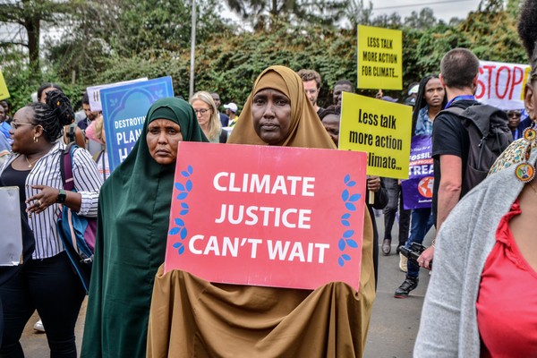 Kenianische Klimaaktivistinnen halten Schild mit der Aufschrift "Climate justice can't wait" hoch.