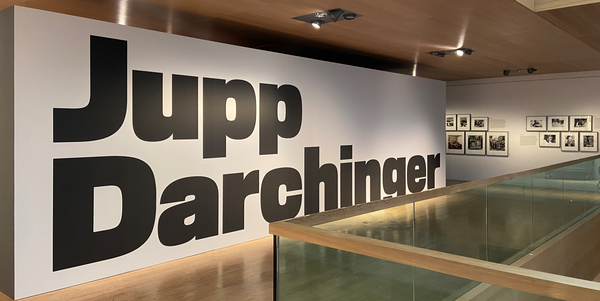 Blick in den Ausstellungsbereich der Darchinger-Ausstellung. Auf einer großen weißen Wand steht der Name "Jupp Darchinger"