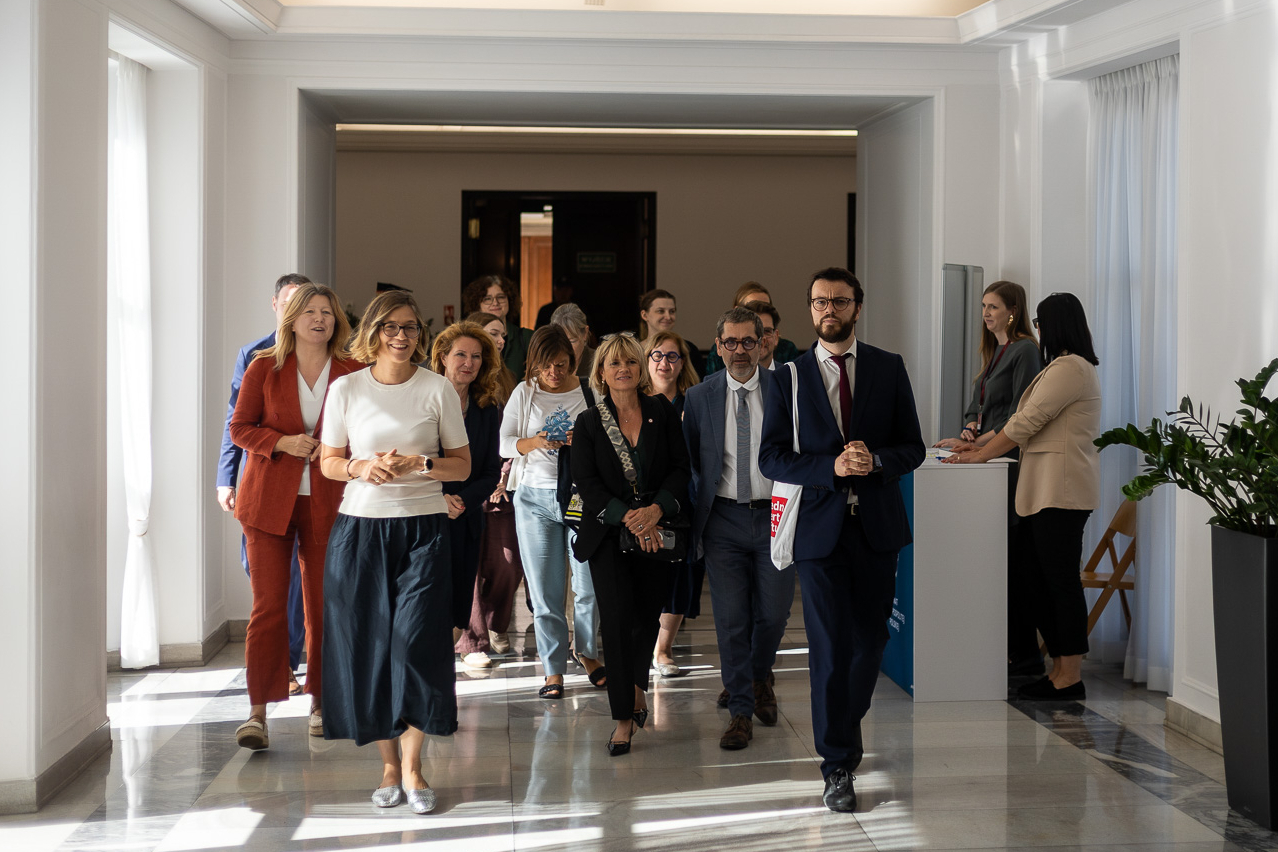 Eine Gruppe von Frauen und Männern geht gemeinsam durch einen hellen Flur, einige im Gespräch