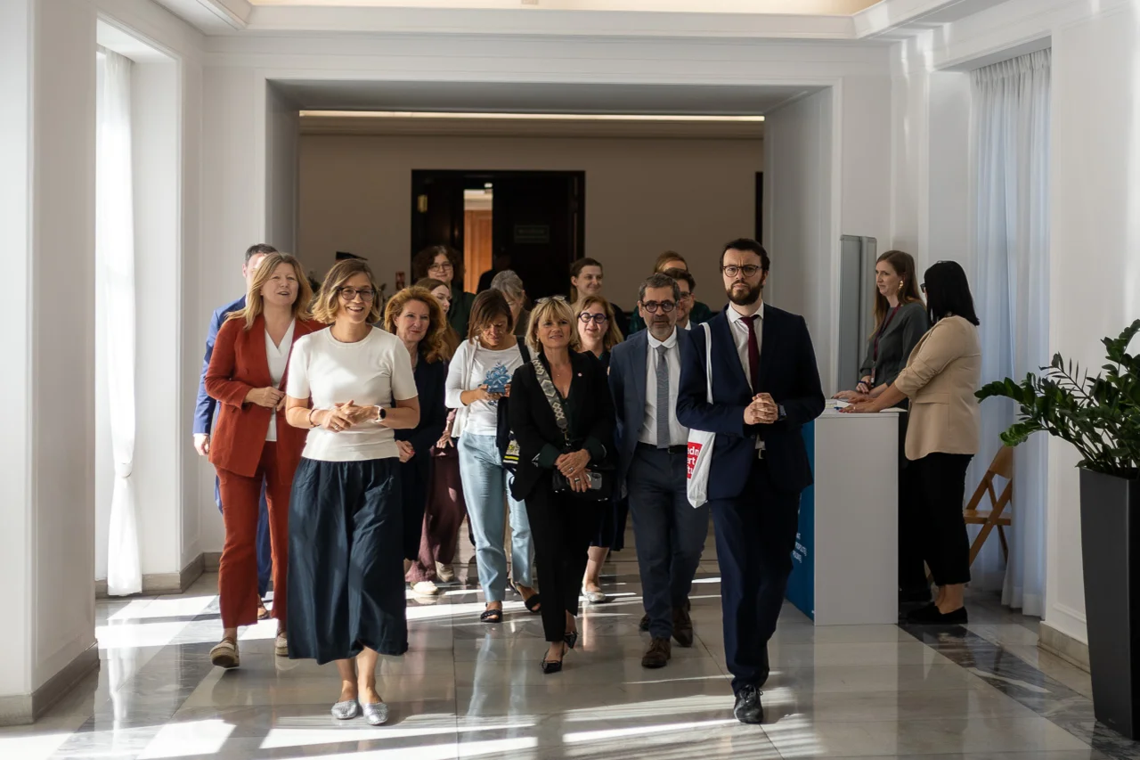 Eine Gruppe von Frauen und Männern geht gemeinsam durch einen hellen Flur, einige im Gespräch