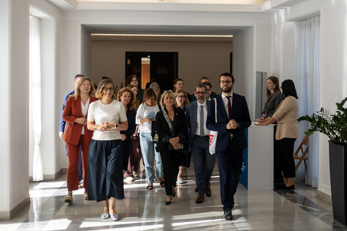 Eine Gruppe von Frauen und Männern geht gemeinsam durch einen hellen Flur, einige im Gespräch