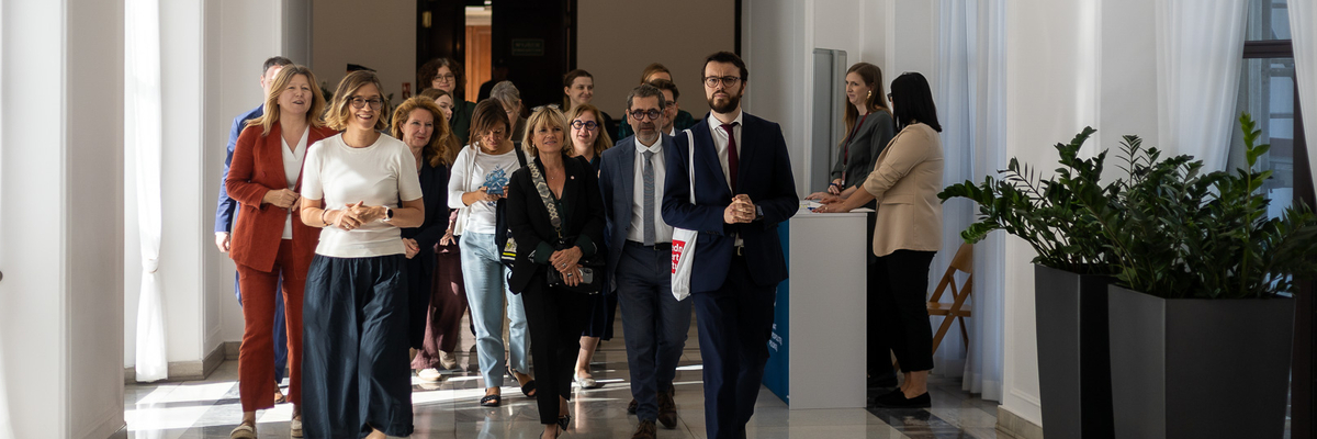 Eine Gruppe von Frauen und Männern geht gemeinsam durch einen hellen Flur, einige im Gespräch