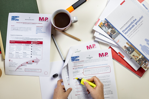 Ein Tisch mit Materialien der MuP-Praxishilfe. Ein Person markiert einen Absatz in einem Dokument.