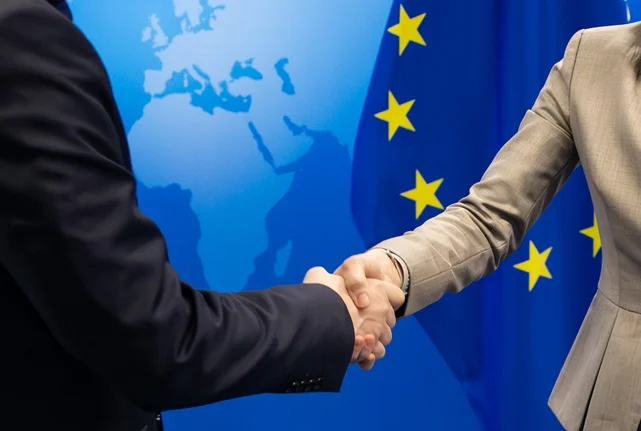 Handschlag vor Europaflagge und Grafik einer Weltkarte.