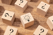 Viele Holzwürfel mit Fragezeichen, in der Mitte ein Holzwürfel mit einer Glühbirne