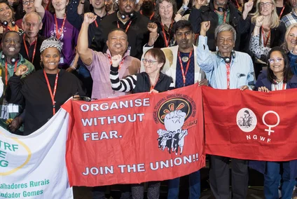 Eine Gruppe von Gewerkschafter:innen hält Banner und Schilder hoch, um ihre Botschaften "Organize without fear" während einer Versammlung zu verbreiten. 